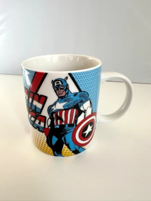Captain America mugg Marvel - Cool mugg med Captain America-motiv i färgglad serietidningsstil. Muggen är vit med tryck i blått, rött, svart och gult och har texten 'Captain America' samt en stor bild av superhjälten. Perfekt för Marvel-fans som vill ha något unikt till kaffet eller teet.