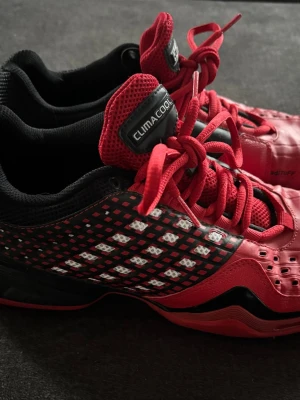 Adidas ClimaCool röda sneakers - Snygga Adidas ClimaCool sneakers i rött och svart med vita detaljer. Skorna har ventilerande meshpaneler, röda skosnören och svart innersula. Märkta med adiTUFF på sidan och Adidas-logga på hälen. Perfekta för dig som gillar sportig och cool stil.