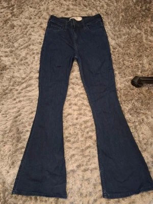Mörkblå utsvängda jeans - Säljer ett par mörkblå jeans med utsvängda ben, perfekta för dig som gillar retrostil. Jeansen har hög midja och klassisk femficksdesign. Materialet är denim i bomull och passformen är figurnära upptill med breda ben nertill.