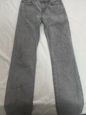 Grå raka jeans i tvättad denim - Säljer ett par grå jeans med rak passform och klassisk femficksdesign. Jeansen har en tvättad look och är tillverkade i denim, vilket ger en avslappnad vibe. Perfekta för dig som gillar stilrena och tidlösa plagg.