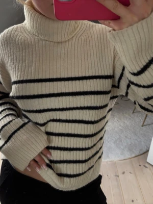 Randig polotröja i offwhite och svart - Stickad polotröja i offwhite med svarta horisontella ränder. Tröjan har ribbstickad struktur, långa ärmar och hög polokrage. Använd fåtal gånger. Skriv för fler frågor 💞