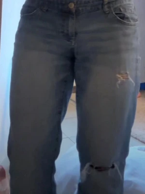 Lågmidajde lösa jeans med hål  - Ett par blå jeans med raka ben och flera slitningar samt hål på låret och knät. På första bilden så gar hålet på låret blivit större ( som visas på andra bilden). Jätte fina och sitter löst hela vägen ner på mig som är på bilden 