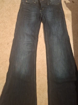 Mörkblå bootcut jeans - Säljer ett par mörkblå bootcut jeans med klassisk femficksdesign och lätt slitningar framtill. Jeansen har normal midja och vida ben, perfekta för en avslappnad och trendig look. Materialet är denim i bomull för skön känsla.