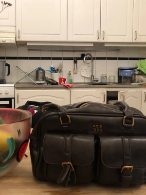 Mörkbrun handväska från COIH 2DN - Snygg mörkbrun handväska i läderlook från COIH 2DN. Väskan har två stora framfickor med spännen i guld och dragkedja upptill. Praktiska handtag och detaljer i guld. Trasigt spänne men går nog att laga! Perfekt för dig som vill ha både stil och funktion. Skriv för funderingar💐💐