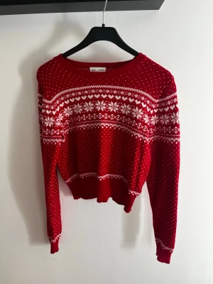 Röd jultröja från Holly & Whyte - Röd stickad tröja från Holly & Whyte by Lindex med vitt vintermönster och snöflingor. Tröjan har rund hals, långa ärmar och ribbade muddar. Perfekt för vintersäsongen och julens mysiga dagar. Säljes för den är för liten. 