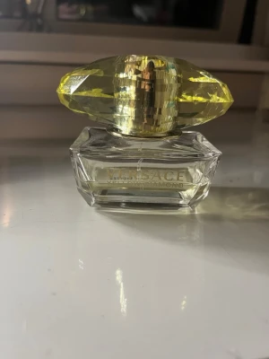 Versace Yellow Diamond parfym - Versace Yellow Diamond parfym i en elegant glasflaska med en stor, gul, diamantformad kork. Flaskan är transparent och har guldfärgad text på framsidan. Perfekt för dig som gillar lyxiga och fräscha dofter. 30% kvar
