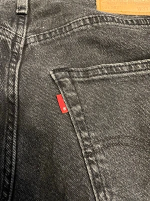 Svarta Levi's 502 jeans - Säljer ett par svarta Levi's 502 jeans med klassisk femficksdesign och rakt ben. Jeansen har den ikoniska röda Levi's-lappen på bakfickan och patch i läder bak i midjan. Tillverkade i slitstarkt denimtyg som ger en snygg och avslappnad look.