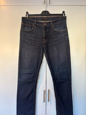 Nudie jeans Grim Tim 34/34 - Nudie Jeans Grim Tim 34/34  Snygga slim fit jeans i mörkblå färg. Bra skick och sitter riktigt bra. Funkar till både vardag och lite finare tillfällen.  Säljes då de inte används längre. Hör av dig vid frågor eller om du vill ha fler bilder!