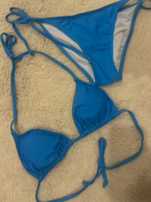 Blå trekantsbikini med knyt - Snygg blå bikini med trekantsmodell och knyt i både topp och trosa. Klassisk design som ger en sportig och fräsch look. Perfekt för lata dagar på stranden eller poolen. Materialet känns mjukt och följsamt mot huden. helt ny, aldrig använt.