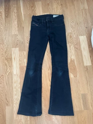 Svarta bootcut jeans från Diesel - Säljer ett par svarta bootcut jeans från Diesel med klassisk femficksmodell och låg midja. Jeansen har en diskret logga på myntfickan och är tillverkade i ett mjukt denimtyg med lätt stretch. Perfekta för dig som gillar en tidlös och avslappnad stil.