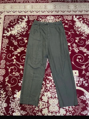 Olivgröna Kostymbyxor - Snygga olivgröna kostymbyxor med klassiskt pressveck och hög midja. Byxorna har en rak passform och stängs med knapp och dragkedja. Mindre skavanker syns på sista bilden (nopprig). 2 för 120 kr på alla herrbyxor. 