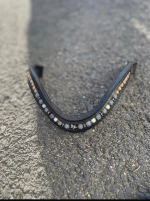 Svart läderpannband med pärlor - Snyggt svart pannband till häst i läder, dekorerat med blå, guldiga och vita pärlor samt glittrande stenar. Perfekt för att ge tränset en extra touch av stil. Passar de flesta träns och är lätt att byta ut. Ursprungspriset är 1199kr. Skriv såklart till mig ifall du har några frågor eller funderingar!❤️🤗