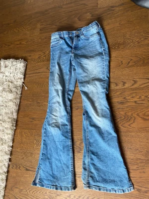 Blå bootcut jeans med slitningar - Ett par blå bootcut jeans med snygga slitningar och lätt tvättad look. Klassisk femficksmodell med normal midja och dragkedja. Perfekta för en avslappnad och trendig stil.