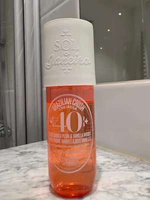 Sol de Janeiro Cheirosa 40 Body Mist - Fräsch body mist från Sol de Janeiro i doften Cheirosa 40 med toner av svart bärnsten, plommon, vaniljträ och jasmin. Flaskan är cylinderformad i orange plast med vit kork och tydlig logga. Perfekt för dig som gillar söta och lyxiga dofter. 240ml, se hur mycket som är kvar på bilden 