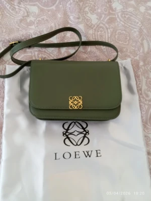 Olivgrön Goya classic bag från Loewe - Snygg olivgrön axelväska från Loewe i slätt skinn med guldfärgad logodetalj framtill. Väskan har justerbar axelrem och stilren, boxig form. Perfekt för dig som vill ha en trendig och exklusiv accessoar med minimalistisk design.
