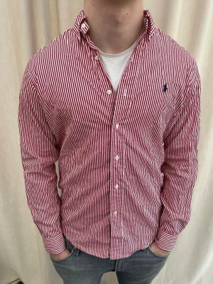 Rödvit randig skjorta från Ralph Lauren - Riktigt snygg randig skjorta från Ralph Lauren. Strl M, personen på bilden är 184 cm lång. Skicka gärna prisförslag. Kika in min profil för mer schyssta plagg.