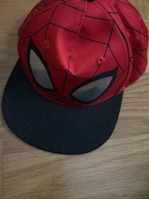 Röd Spiderman-keps från H&M - Cool röd keps från H&M (barnavdelning men passar okej på tonåringar också) med Spiderman-design och svarta spindelnätslinjer. 