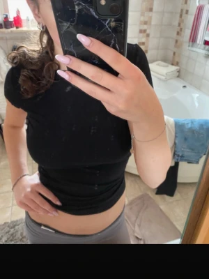 Svart topp med öppen rygg - Säljer en svart, tight topp med korta ärmar och en riktigt snygg öppen rygg. Toppen är croppad och har en stilren, enkel design som passar perfekt till jeans eller kjol. Materialet känns mjukt och stretchigt, passar både till vardag och fest!