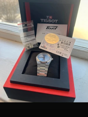 Tissot PRX Quartz 35mm - Snygg Tissot PRX klocka i silver med stilren länk i rostfritt stål och ljusblå urtavla. Kommer i originalask med extra länkbitar och certifikat. Perfekt accessoar för dig som gillar klassisk och modern design.