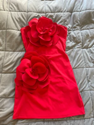 Röd kort klänning med stora blommor - Supersnygg röd kort klänning med två stora blommor framtill. Använd en gång på tema Capitol fest!!🥰