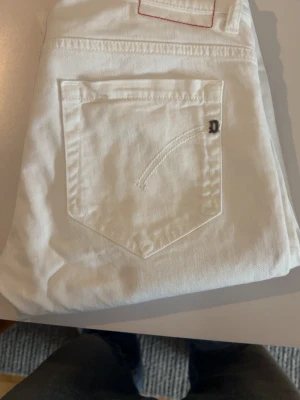 Vita jeans från Dondup - Säljer ett par vita jeans från Dondup med klassisk femficksmodell och knappgylf. Jeansen har en diskret logga på bakfickan och är tillverkade i ett mjukt bomullsmaterial. Perfekta för en clean och fräsch look.