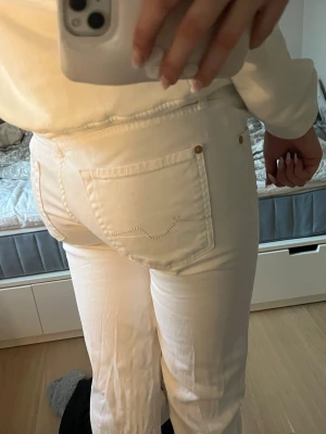 Vita jeans med detaljer - Säljer ett par vita jeans med snygga sömdetaljer på bakfickorna. Jeansen har klassisk femficksmodell, gylf med dragkedja och knapp samt guldfärgade nitar. Perfekta för dig som vill ha en clean och fräsch look.
