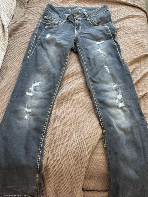 Lågmidjade jeans - Säljer ett par blå jeans från SoSoWear med slitna detaljer och kontrastsömmar. Jeansen har låg midja. Midjemått rakt över: 37 men de är väldigt stretchiga material. Innerben:75cm. Jag hittar inte vart storleken står men gissar på typ storlek 36-38