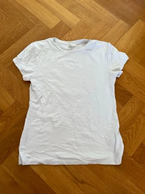 Vit basic t-shirt i polyester  - En enkel vit t-shirt i mjuk bomull med rund hals och korta ärmar. Perfekt till jeans eller shorts för en clean och avslappnad stil. Klassisk passform utan tryck eller detaljer.