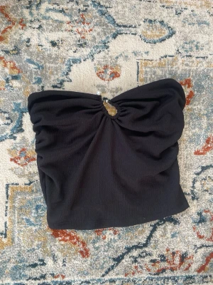 Svart bandeau tubtopp med pärlor - Säljer en svart bandeau tubtopp med snygg rynkning och dekorativa pärlor framtill. Materialet är ribbad och känns mjukt mot huden. Den är disket men ändå unik men en extra touch! Den har en bra passform och är perfekt för en utekväll! Har inte fått tillfälle att använde väljer därför att sälja.🌹