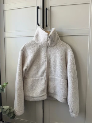 Vit teddyjacka H&M - Mysig cremevit teddyjacka med dragkedja framtill och hög krage. Perfekt nu till våren. Knappt använd så väldigt bra skick. Från H&M men finns inte att köpa längre.