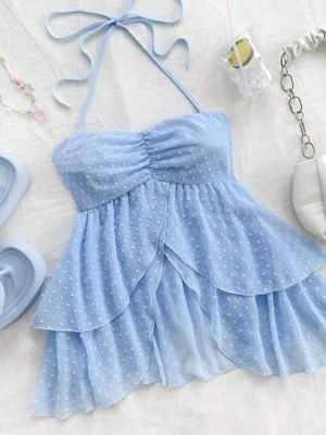 Ljusblå volang topp med halterneck - Supersöt ljusblå topp med volanger och halterneck-knyt. Toppen är ärmlös och har ett prickigt mönster i tyget samt smock i ryggen för skön passform. Perfekt för sommarens alla tillfällen och ger en romantisk vibe.