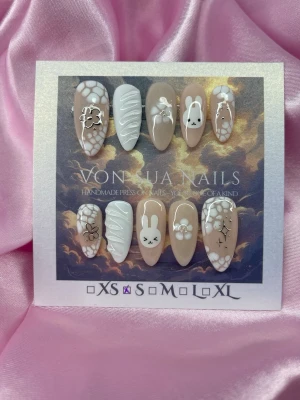 CreamMiffy (S);Medium Almond - Handgjorda press-on naglar i en medium mandelform. Designen är beige och vit med söta (Miffy) kaninmotiv,-blommor och detaljer i silver. Perfekt för dig som vill ha unika och kreativa naglar med gulliga inslag. S: 15 mm, 11,5 mm, 12 mm, 11 mm, 9 mm 