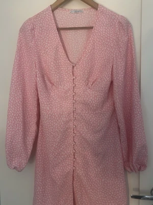 Rosa Adoore liknande klänning - Supersöt rosa klänning från Nelly med vita leopard mönster, v-ringad hals och långa ärmar. Klänningen har dekorativa knappar framtill. Perfekt till sommaren!  Den är i storlek 36 som motsvarar S, säljer då den inte kom till användning! Inga defekter💗