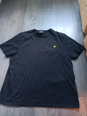 Svart t-shirt med gul logga - Svart t-shirt med rund hals och en liten gul logga på bröstet. Klassisk passform och tillverkad i mjukt bomullstyg. Perfekt för en stilren och enkel look. Använd 1 gång 