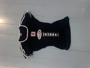 Svart t-shirt med vita detaljer - Snygg vintage svart t-shirt med vita kanter vid ärmar och hals. Framsidan har tryck med text och siffror i vitt och rött. T-shirten har en figurnära passform och korta ärmar. 