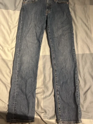 Klassiska raka blå Levi's jeans - Säljer ett par klassiska blå jeans från Levi's med rak passform och fem fickor. Jeansen har tydliga sömmar, normalhög midja och är tillverkade i slitstark denim. Perfekta för en avslappnad och tidlös stil.