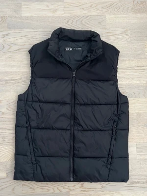 Zara väst - Svart, S - Svart väst från Zara. Mycket bra skick utan tydliga tecken på användning. Västen är gjord i nylon och polyester. Två sidofickor med dragkedjeknäppning. Normal passform.