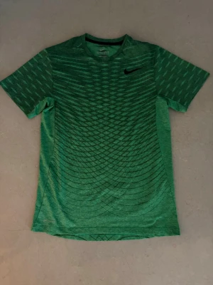 Grön Nike t-shirt med mönster - Snygg grön t-shirt från Nike med svart logga på bröstet och ett coolt geometriskt mönster över hela tröjan. T-shirten har korta ärmar och är tillverkad i ett lätt och andningsbart material, perfekt för träning eller vardagsstil. Tishan är använd för ett fåtal gånger och fungerar felfritt. ABS! Pris går att diskutera!
