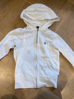Vit hoodie från Polo Ralph Lauren - Snygg vit hoodie med dragkedja från Polo Ralph Lauren i storlek S. Tröjan har tecken på användning då jag själv köpt den begagnat - se två sista bilderna - även luvan är något nopprig. Pga detta vet jag inte heller om den är äkta, därav priset🤍