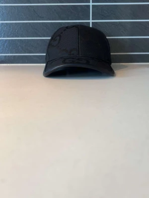 GG KEPS - Snygg svart keps med det klassiska GG-mönstret över hela kepsen. Kepsen har böjd skärm och är tillverkad i ett tåligt tygmaterial med detaljer i svart. Perfekt accessoar för en trendig och stilren look.