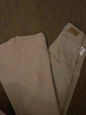 Beiga raka jeans med hög midja - Säljer ett par beiga jeans med rak passform och hög midja. Jeansen har klassiska bakfickor och bälteshällor. Materialet är kraftigt och känns som bomull, perfekta till en avslappnad stil.