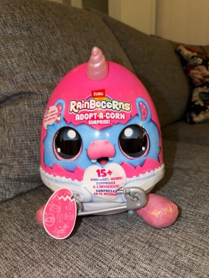 NY! Rainbocorns Adopt-A-Corn Surprise - Rainbocorns Adopt-A-Corn Surprise är ett ägg med över 15 överraskningar. Inuti finns en mjukdjursfigur och tillbehör. Det finns 7 olika figurer att samla på. Ny oöppnad!