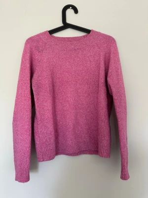 Rosa stickad tröja med rund hals - Mysig rosa stickad tröja med rund halsringning och långa ärmar. Tröjan har ribbstickade muddar vid ärmslut och nederkant. Perfekt för att hålla värmen under kyliga dagar. Har lite noppror 