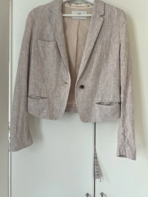 Beige randig kavaj från day - Snygg beige kavaj från day med tunna vita ränder. Klassisk modell med en knapp framtill, två fickor och en bröstficka. Tillverkad i ett lätt tyg som känns luftigt och passar perfekt till vår och sommar. Enkel att styla till olika looks.