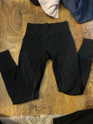 Svarta sömlösa leggings - Säljer ett par svarta sömlösa leggings med hög midja. De är stretchiga och har en ribbad linning för extra komfort. Perfekta till både träning och chill. Materialet känns mjukt och följsamt mot huden. Storlek xs/s