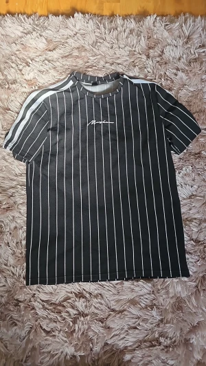 Svart randig t-shirt från SHEIN - Snygg svart t-shirt från SHEIN med vita vertikala ränder och diskret logga på bröstet. T-shirten har korta ärmar och rund halsringning. Perfekt för en avslappnad och trendig stil.