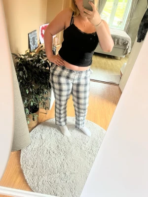Rutiga pyjamasbyxor i svart och vitt - Säljer ett par pyjamasbyxor med svartvitt rutmönster och dragsko i midjan. Byxorna har raka ben och är tillverkade i ett mjukt, bekvämt material som passar perfekt för hemmamys och avslappning.