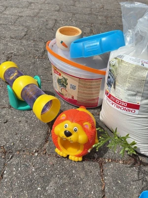 Tillbehörspaket för smådjur - Säljer ett paket med smådjurstillbehör: en stor hink med lock, en påse chinchillasand (5 kg), en gul-orange leksak i form av ett lejon, ett gult och blått plasttunnelrör samt en liten keramikskål med morotsmotiv. Perfekt för dig som har gnagare eller smådjur.
