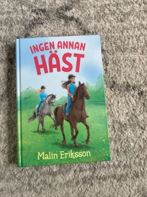 Ingen annan häst av Malin Eriksson - En färgglad bok med hårdpärm, titeln 'Ingen annan häst' av Malin Eriksson. Omslaget visar två tjejer som rider hästar på en grön äng, med blå himmel och träd i bakgrunden. Perfekt för dig som gillar hästar och spännande berättelser.