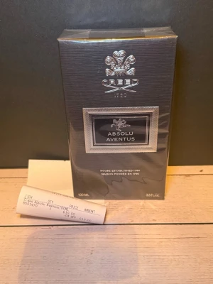 Creed Absolu Aventus 100ml parfym - Lyxig parfym från Creed, modellen Absolu Aventus i 100ml flaska. Förpackningen är elegant och svart med silverdetaljer och Creed-loggan i silver. Perfekt för dig som gillar exklusiva dofter och snygg design.